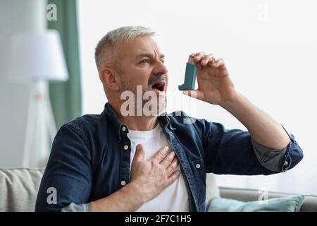 Senior man touching chest and using inhaler Stock Photo