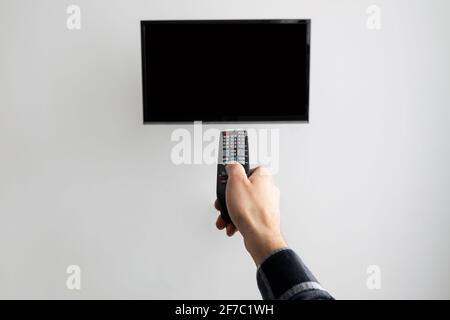 Hand Pointing Controller At Blank TV Screen On Wall Indoor Stock Photo