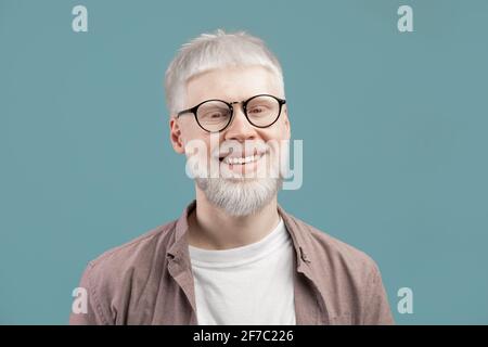 Headshot portrait of happy man with pale skin wearing eyeglasses, looking and smiling at camera on turquoise background Stock Photo
