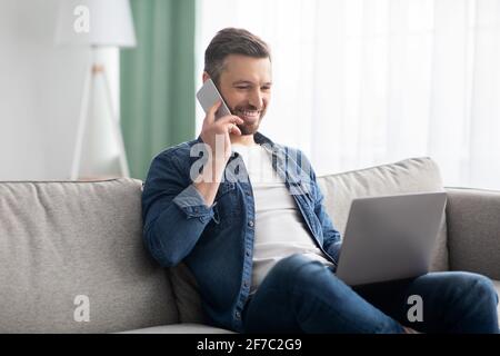Happy middle-aged man with laptop talking on smartphone Stock Photo