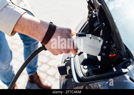 Man inserts plug of the charger into the socket of electric car close-up Stock Photo