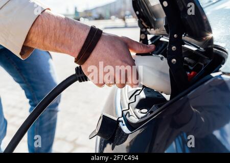 Man inserts plug of the charger into the socket of electric car close-up Stock Photo