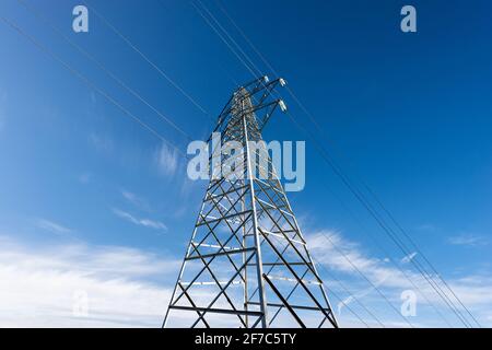 Photography of a High voltage tower, power line with electric cables and insulators against a blue sky with clouds and copy space. Stock Photo