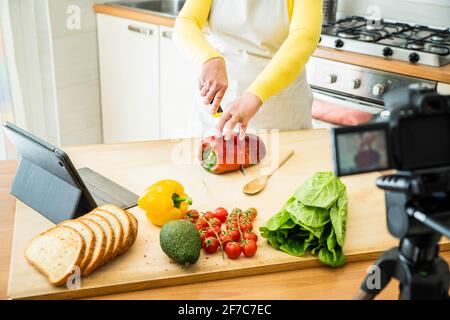 Woman cooking healthy food in the kitchen - Food blogger recording video tutorial at home - People, food and blogger concept Stock Photo