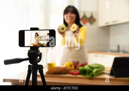 Woman cooking healthy food in the kitchen - Food blogger recording video tutorial at home - People, food and blogger concept Stock Photo