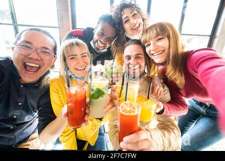 Multiracial people wearing protective face masks drinking cocktails at bar restaurant - New normal friendship concept with young friends taking a self Stock Photo