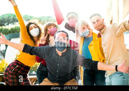 Group of multiracial people wearing protective face masks smiling at camera - New normal friendship concept with multicultural friends having fun outd Stock Photo