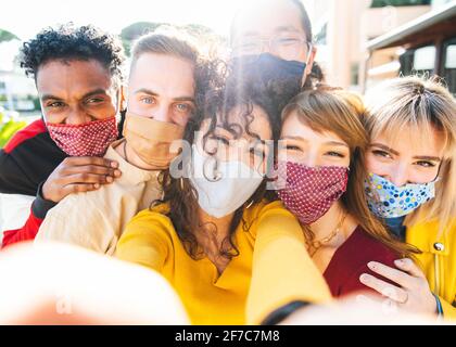 Happy friends wearing face masks taking a selfie outdoor - New normal friendship concept with young people having fun in the city - Main focus on cent Stock Photo