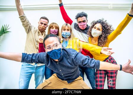 Multicultural people covered by protective face masks smiling at camera - New normal friendship concept with young friends having fun outdoor - Bright Stock Photo