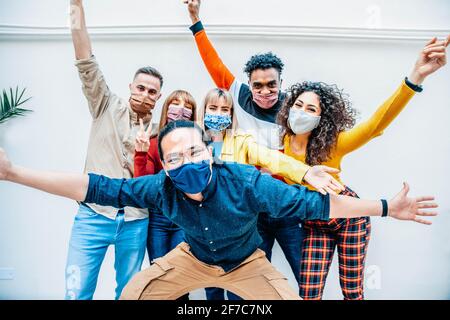 Multicultural people covered by protective face masks smiling at camera - New normal friendship concept with young friends having fun outdoor - Bright Stock Photo