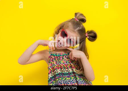 Cute little girl in sun glasses on the yellow background in the studio. Stock Photo