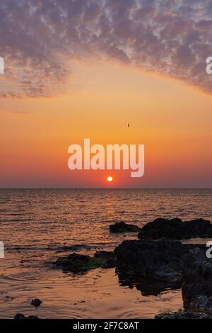 Orange sunset on the sea. Bright juicy landscape with cirrus clouds on the horizon. Purple, lilac and pink shades of the evening sky. The smooth surfa Stock Photo