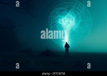 A science fiction concept. Of a man with a torch looking at an alien in the sky, in a field on a misty winters night. Stock Photo