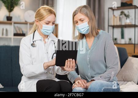 Elderly people healthcare concept. Female professional doctor using digital tablet app, showing medical test result, explaining prescribed medicines, while visiting senior woman patient at home Stock Photo