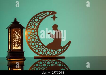 Eid Mubarak concepts with lamp inscribed with arabic text translated to english as Ramadhan is our light., with crescent moon in silhouette Stock Photo