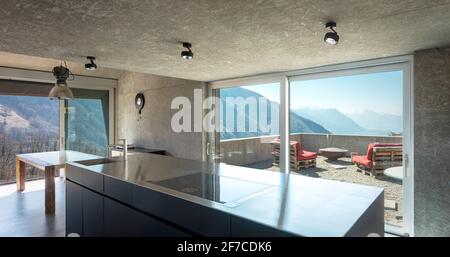 Modern white kitchen with large island, induction hob, sink and stainless steel top. Large windows overlooking the nature of Switzerland. Nobody insid Stock Photo