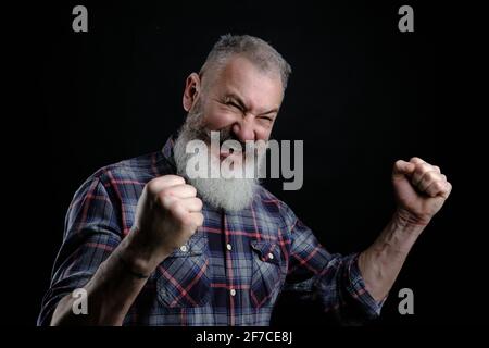 Portrait of happy joyful and emotive bearded mature european guy, raising fists high and yelling, triumphing or cheering while watching football match Stock Photo