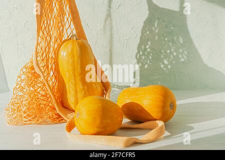 Orange pumpkins in an eco-friendly string bag on a wooden table. A festive composition for Thanksgiving. Conceptual bright design for Halloween. Natur Stock Photo