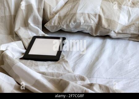 A modern black electronic book with a blank screen on a white and beige bed. Mockup tablet on bedding Stock Photo