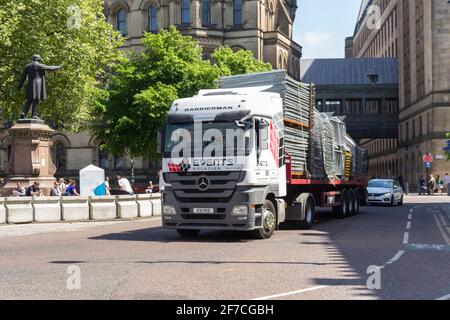 A Mercedes-Benz Actros 1844 truck hauls an articulated flat trailer carrying portable crowd control barriers away from Albert Square, Manchester. Stock Photo