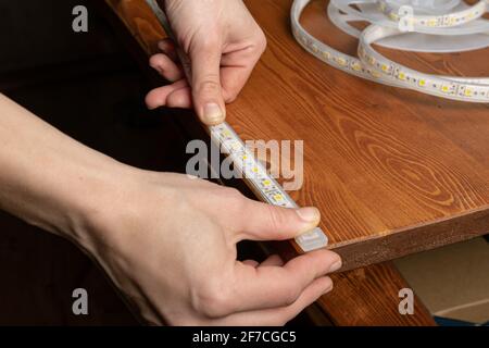 the master glues the LED strip into the niche of the shelf from the cabinet Stock Photo