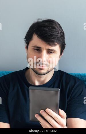 Handsome man is reading a gray electronic book. Male with a tablet in his hand. Vertical photo Stock Photo