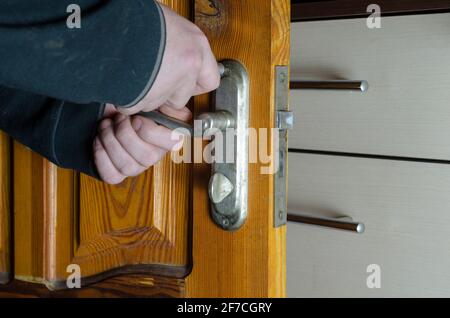 A man removes the old door lock. Hands with a screwdriver unscrew the mounting screws of the mortise lock of a wooden interior door. Services to repai Stock Photo