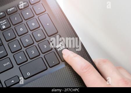 Keyboard corner of a black laptop, lit by sunlight, with a female finger clicking on a don't panic button. The concept of spreading positive news Stock Photo