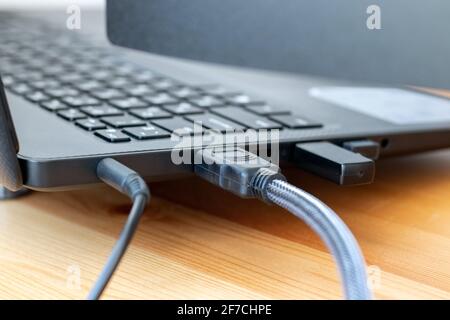 Power and hdmi cables, and wireless dongle USB mouse receiver on the side of a gray laptop on a wooden table. Selective focus. Closeup view Stock Photo