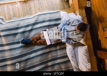 Man in cozy clothes working on laptop while sitting on the bed Stock Photo
