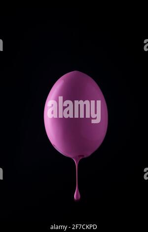 pink egg with paint dripping down. on a black background. minimalistic easter egg close up. Stock Photo