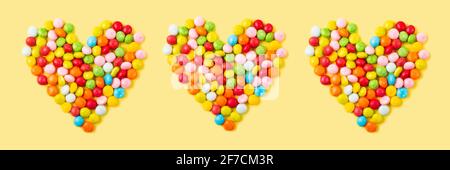 Old fashion pale multi colored candy hearts background on yellow. Banner Stock Photo