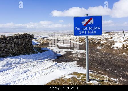 The Pennines in winter - A Do Not Follow Sat Nav sign for lorries on a track in a snowy landscape near Nenthead, Cumbria UK Stock Photo