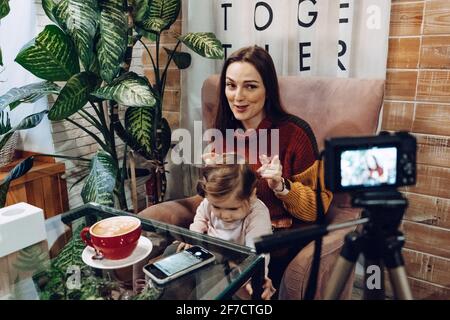 Blogger mother and her little daughter have fun together with the vlog camera. Young parenting blogger recording a video with her baby at home Stock Photo