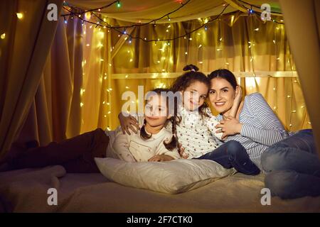 Happy mother and daughter children hugging sitting together in tent home Stock Photo