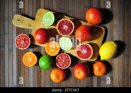 Red sicilian oranges, lime, lemon and mandarine tangerine on cutting board wooden background Stock Photo