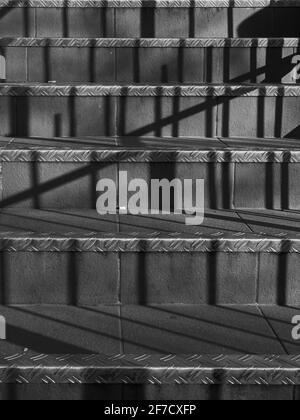A mundane set of ceramic-tiled stairs in close up, rendered abstract by the sharp bars of shadow cast by the strong spring sunshine. Stock Photo
