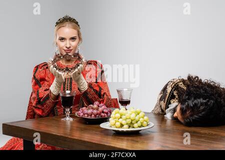 blonde queen looking at poisoned hispanic king in medieval clothing choking isolated on white Stock Photo
