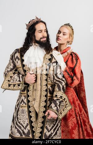 blonde queen in royal crown hugging hispanic king in medieval clothing isolated on white Stock Photo