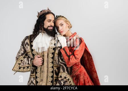 blonde queen in crown hugging hispanic king in medieval clothing isolated on white Stock Photo