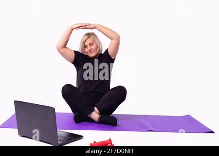 Sporty senior woman warming up stretching watching fitness video tutorial on laptop, fit woman doing workout at home sitting on mat in living room Stock Photo