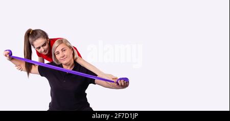 Banner- long format. Powerful attractive female fitness senior woman using resistance band training body with her workout teacher, trainer at home Stock Photo