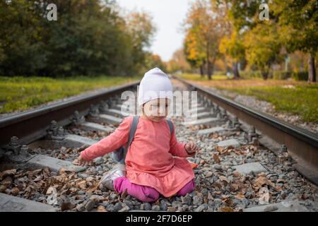 little girl sitting on the railroad tracks. toddler plays on railroad in forest Stock Photo