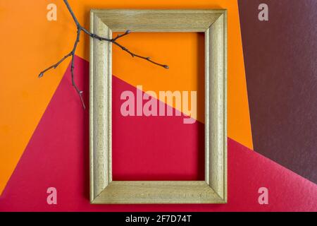 Empty wooden frame made of beech and tree branch without leaves on multi-colored abstract paper background. Red, orange, brown. Place for photo. Stock Photo