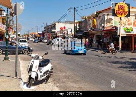 Zakynthos, Greece - August 14, 2016: White scooter is parked on the street of Laganas resort town. Ordinary people walk the street Stock Photo