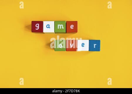 Words Game Over made from colored wooden blocks. They are arranged in two rows. Painted cubes with letters on yellow background. Top view. Stock Photo