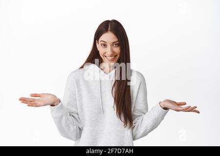 So what, I have nothing. Smiling unbothered girl smiling with cunning sly look, spread hands sideways and shrugging careless, dont care, feel relaxed Stock Photo