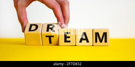 Dream team symbol. Businessman turns cubes and changes the word 'dream' to 'team'. Beautiful yellow table, white background. Business and dream team c Stock Photo