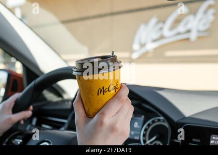 Woman sitting in the car and drinking coffee from McCafe, April 2021, Prague, Czech Republic.  Stock Photo