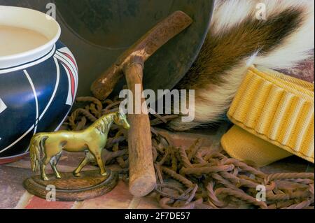 Old West closeup display. Horse statue, Native American pottery, gold pan with pick axe, deer tail, ammo belt and old rusty chain. Museum collection. Stock Photo